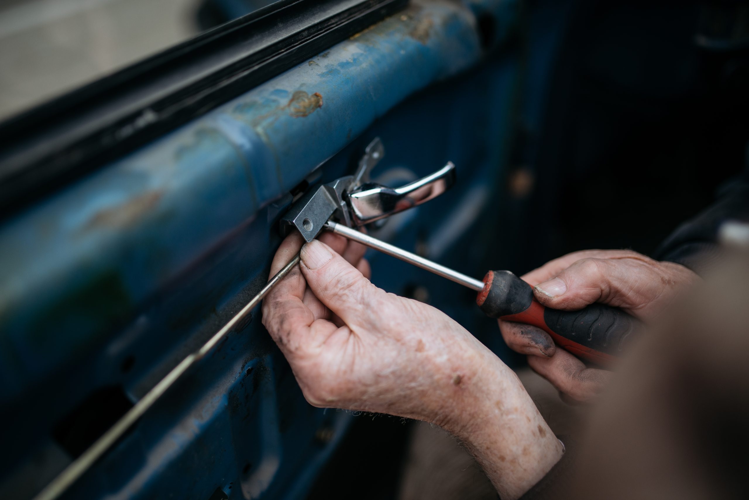 Twee handen die met een schroevendraaier een deurslot van een auto afstellen